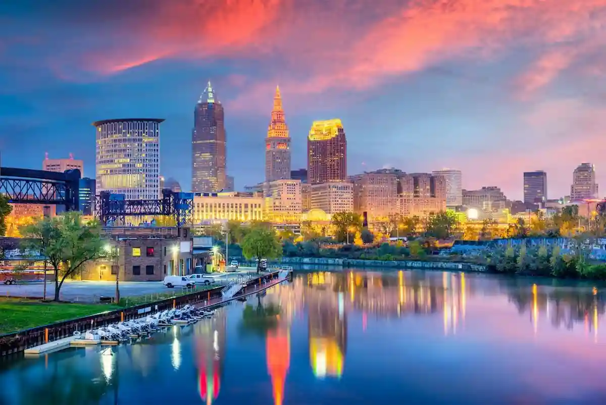  A stunning panoramic view of Cleveland, Ohio, at sunset. The city's skyline is illuminated by the vibrant colors of the sky, reflecting in the calm waters of the river below. The iconic Key Tower stands tall, dominating the cityscape.